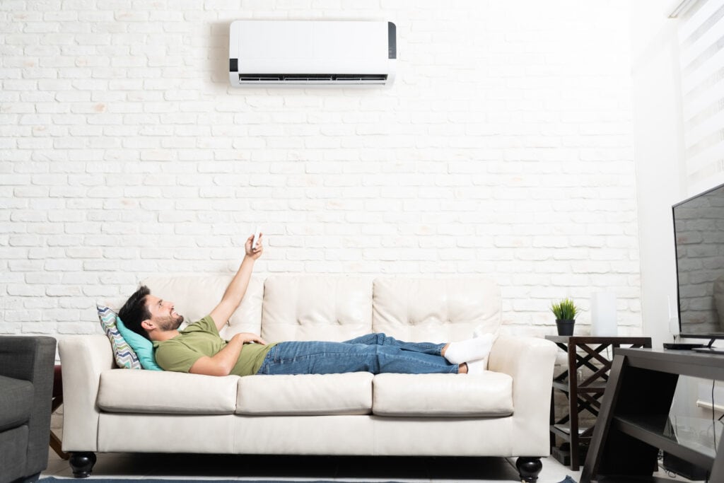 Man turning on ductless mini split AC while relaxing on sofa at home in Edmonton